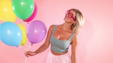 Gözlüklü, pembe arka planda renkli balonları olan gülümseyen kadın.