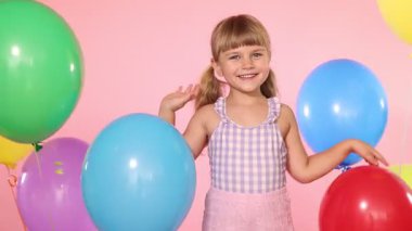 Pembe arka planda bir sürü renkli balonu olan neşeli küçük kız.