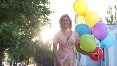 Gün batımında açık havada renkli balonlarla gülümseyen kadın, kamera hareket ediyor.