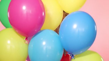 Pembe arka plandaki renkli balonların arasında gülümseyen küçük kız.