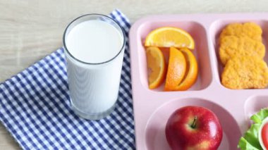 Okul yemeği. Lezzetli yiyecek, süt ve çatal içeren plastik tepsi, ahşap masa, yakın çekim. Kamera sağa hareket ediyor