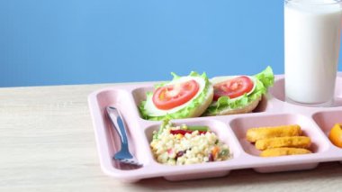 Okul yemeği. Lezzetli yiyecek, süt ve çatal içeren plastik tepsi, ahşap masa, yakın çekim. Kamera sağa hareket ediyor