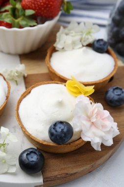 Lezzetli tatlı. Kremalı tartlar, böğürtlenler ve çiçekler beyaz döşemeli masada, yakın plan.