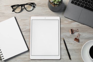 Tablet, farklı kırtasiye malzemeleri, gözlükler, bilgisayar klavyesi ve ahşap masa üzerindeki çiçek dekoru.