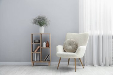 Rahat koltuk ve ahşap raf. Açık gri duvarın yanında farklı dekorlar var.