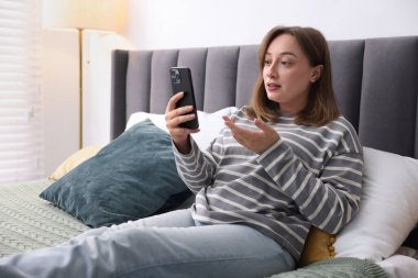 Bir kadın, kapalı bir odada, akıllı telefondan doktorla çevrimiçi istişare ediyor.