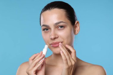 Açık mavi arka planda dudak merhemi olan genç bir kadın.