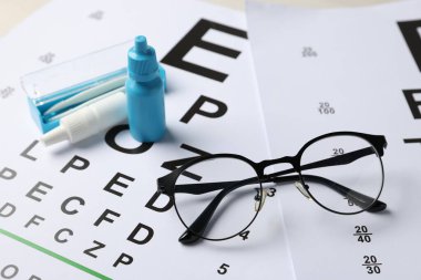 Gözlükler, tıbbi damlalar ve cımbızlar görüş test çizelgelerinde, yakın plan.