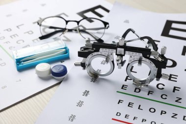 Görüş test çizelgeleri, deneme çerçevesi, gözlükler, cımbız ve lensler masada, yakın plan