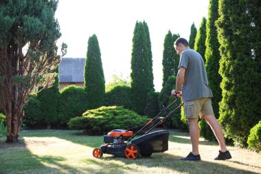 Bahçede çim biçme makinesiyle yeşil çim biçen bir adam
