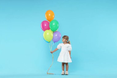 Açık mavi arka planda bir sürü renkli balonu olan şirin bir kız.