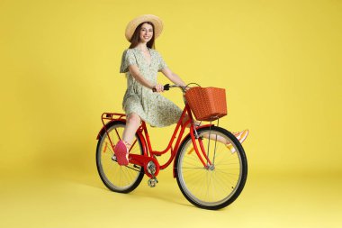 Açık yeşil arka planda sepeti olan şapkalı, gülen bir kadın.