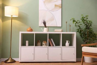 İçerideki yeşil duvarın yanında dekoratif elementlerle, lambayla ve bitki örtüsüyle raf ünitesi.