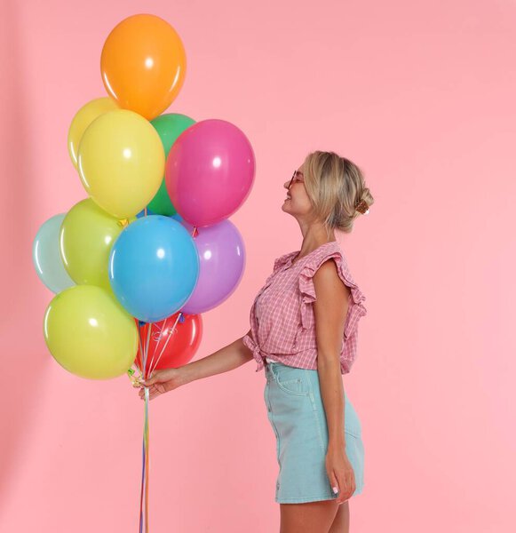Smiling woman in sunglasses with bunch of colorful balloons on pink background