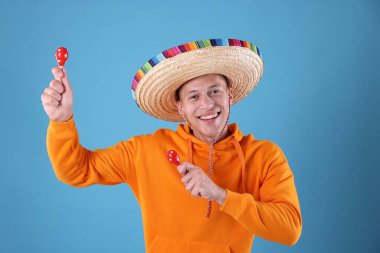 Şapkalı mutlu adam açık mavi arka planda marakas çalıyor.