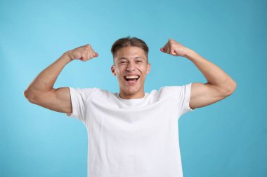 Kuvvet. Kaslarını açık mavi arka planda gösteren mutlu bir adam.