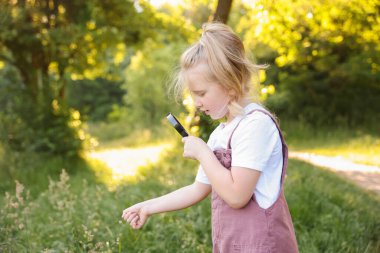 Doğadaki büyüteçten bitkilere bakan sevimli küçük kız.