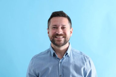 Yakışıklı adam açık mavi arka planda gülüyor.