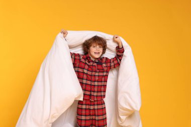 Sarı arka planda battaniyesi olan pijamalı şirin bir çocuk.