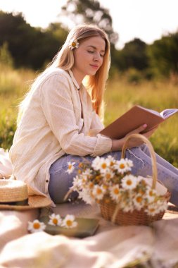 Bir buket kır çiçeğiyle çayırda kitap okuyan güzel bir kadın.