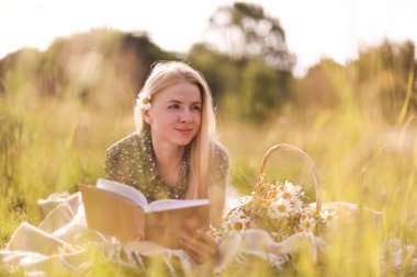 Bir buket kır çiçeğiyle çayırda kitap okuyan güzel bir kadın.