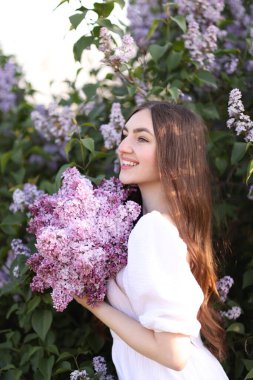 Leylak çiçeklerinin arasında gülümseyen ve açık havada terk eden kadın.