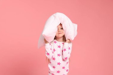 Pembe arka planda yastıklı pijamalı şirin bir kız.