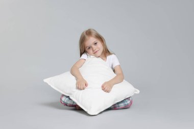 Gri arka planda yastıklı pijamalı şirin bir kız.