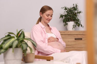 Evdeki koltukta oturan güzel hamile kadın.