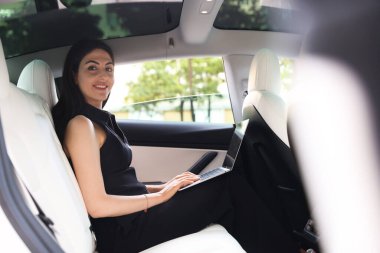 Modern arabada dizüstü bilgisayar kullanan bir kadın. Dışarıdan görünüyor.