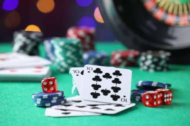 Kumarhane fişleri, zarlar ve iskambil kartları yeşil masada bulanık ışıklara karşı, yakın plan