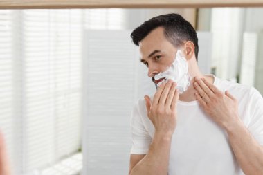 Banyoda aynanın yanında tıraş köpüğü kullanan yakışıklı bir adam. Metin için boşluk