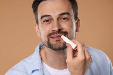 Yakışıklı bir adam açık kahverengi arka planda dudaklarına merhem sürüyor.