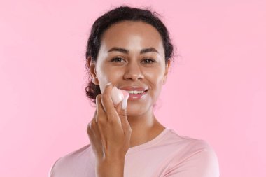 Gülümseyen kadın pembe arka planda dudaklarına merhem sürüyor.