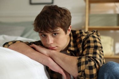 Gençlik sorunları. Evde yatağın yanında üzgün bir genç çocuk var.