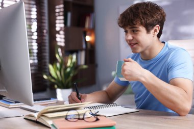 İçki içen genç öğrenci içeride ders çalışırken not alıyor.