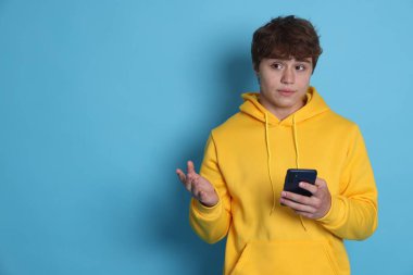 Açık mavi arka planda akıllı telefonu olan genç bir çocuk. Metin için boşluk