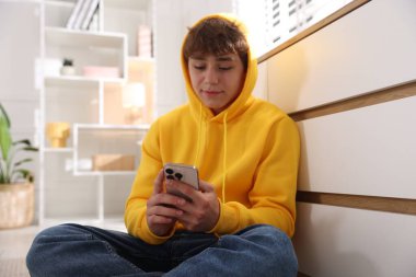 Ergen çocuk evde çekmecelerin yanında akıllı telefon kullanıyor.