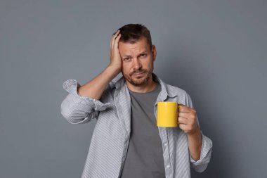 Gri arka planda içki mahmurluğu çeken bir adam.