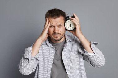 Çalar saati olan bir adam gri arka planda akşamdan kalma.