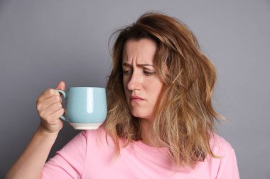 Gri arka planda akşamdan kalma kahve içen bir kadın.