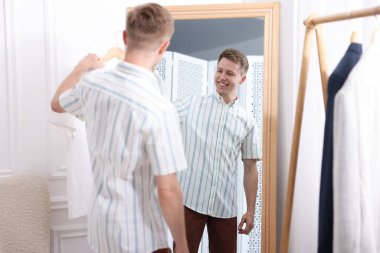 Hazırlanıyor. Genç adam aynanın yanında kıyafet deniyor.