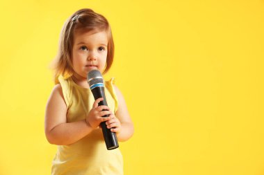 Sarı arka planda mikrofonu olan şirin küçük kız, mesaj için yer var.