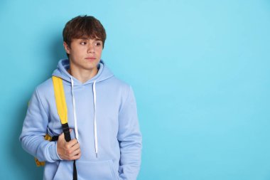 Açık mavi arka planda sırt çantası olan sevimli genç bir çocuk. Metin için boşluk