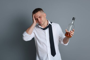 Gri arka planda akşamdan kalma viski şişesi olan bir adam.