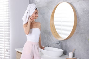 Hazırlanıyor. Evde genç bir kadın aynanın yanında dişlerini fırçalıyor.