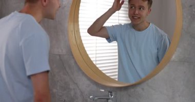 Genç adam evde aynanın yanında hazırlanıyor. Kamera yukarı hareket ediyor