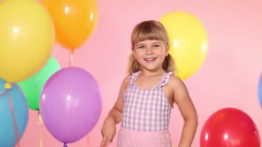 Pembe arka planda bir sürü renkli balonun arasında sevimli küçük kız.