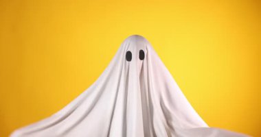 Ürkütücü hayalet. Beyaz çarşaflı adam turuncu arka planda korkunç hareketler gösteriyor.