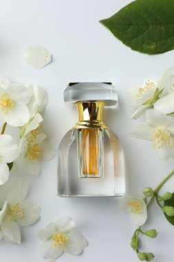 Bir şişe parfüm, yasemin çiçekleri ve beyaz arka planda yeşil yaprak.